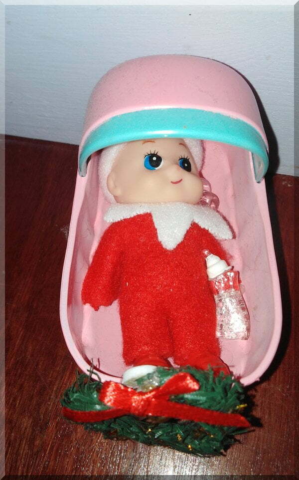 Baby Christmas elf in a cradle with a bottle and dummy