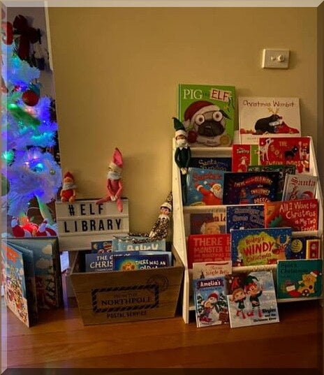 Display of many CHristmas picture books and some elves with a sign "Elf Library"